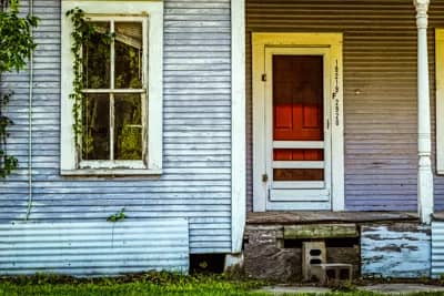 Abandoned House With A Red Door And A Crooked Blind